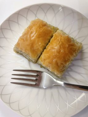 Geleneksel Türk tatlısı. Baklava. İki dilim baklava ve beyaz tabakta bir çatal..