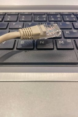 Bir dizüstü bilgisayara bağlanan ethernet kablosu. Bir dizüstü bilgisayarın klavyesindeki RJ45 portuna takılmış bej bir ethernet kablosunu gösteren bir resim. Kablo sarılı ve kısmen klavye tuşlarına bağlı..