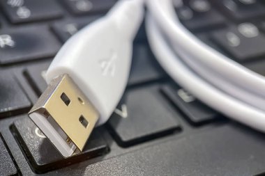 USB kablosunun klavyede yakın plan görüntüsü. Bu resim siyah klavye tuşları üzerinde duran beyaz bir USB kablo konnektörünün yakın plan görüntüsünü içerir. Odak noktası metalik USB konnektörü, parıltısını ve evrensel USB sembolünü gösteriyor.. 