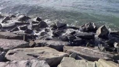 Alacakaranlıkta dalgaların engebeli kayalara nazikçe çarpması. Okyanusun kenarında sakin bir an. Dalgaların ritmik dansı ve kayaların dinginliği..