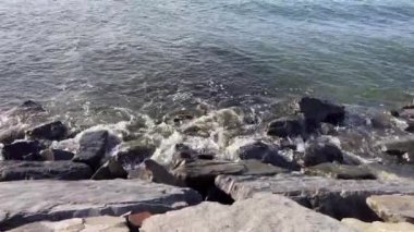 Alacakaranlıkta dalgaların engebeli kayalara nazikçe çarpması. Okyanusun kenarında sakin bir an. Dalgaların ritmik dansı ve kayaların dinginliği..