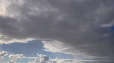 Karanlık ve dönen bulutlarla dolu dramatik bir gökyüzü. Bulutlar hızlı hareket ediyor gibi görünüyor, belki de bir fırtına taşıyor. Karanlık bulutlar ve açık mavi gökyüzü arasında güzel bir kontrastlık var..