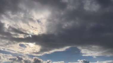 Karanlık ve dönen bulutlarla dolu dramatik bir gökyüzü. Bulutlar hızlı hareket ediyor gibi görünüyor, belki de bir fırtına taşıyor. Karanlık bulutlar ve açık mavi gökyüzü arasında güzel bir kontrastlık var..