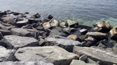 Suyun taşla buluştuğu yerde. Kayalık bir kıyı şeridinin engebeli güzelliği. Karanlık, dokulu taşların, suyun parıldayan yüzeyiyle buluştuğu yerde. Bileşim, kayaların sağlamlığı ile denizin akışkanlığı arasındaki zıtlığı vurgular..  