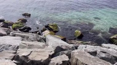 Suyun taşla buluştuğu yerde. Kayalık bir kıyı şeridinin engebeli güzelliği. Karanlık, dokulu taşların, suyun parıldayan yüzeyiyle buluştuğu yerde. Bileşim, kayaların sağlamlığı ile denizin akışkanlığı arasındaki zıtlığı vurgular..  