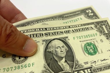 El Tutma Bir ve İki Dolarlık Faturalar 'ın yakın çekimi. İki Amerikan doları banknotunu tutan bir elin detaylı bir yakın çekimi, özellikle bir dolar ve iki dolarlık banknotlar..