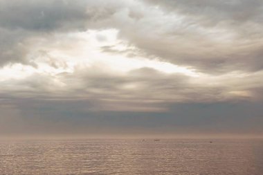 Gün doğumu ve dramatik bulutlar. Baharda sabahın erken saatlerinde sakin deniz manzarası. Huzurlu Bahar Şafağı. Erken bir bahar sabahının huzurlu güzelliğine tanık olun. Güneş yükselir, sakin bir denizin üzerine sıcak bir parıltı saçar dramatik bulutlar gökyüzünü boyarken