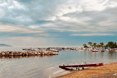 Gün doğumu ve dramatik bulutlar. Baharda sabahın erken saatlerinde sakin deniz manzarası. Huzurlu Bahar Şafağı. Erken bir bahar sabahının huzurlu güzelliğine tanık olun. Güneş yükselir, sakin bir denizin üzerine sıcak bir parıltı saçar dramatik bulutlar gökyüzünü boyarken