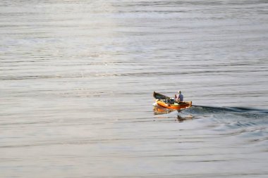 Sakin sularda gün batımına doğru kürek çeken yalnız bir kürekçi, gün batımında huzurlu bir su kütlesinin üzerinde, huzurlu yansımalarla çevrili küçük bir ahşap botta yol alır..