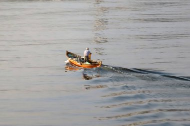 Sakin sularda gün batımına doğru kürek çeken yalnız bir kürekçi, gün batımında huzurlu bir su kütlesinin üzerinde, huzurlu yansımalarla çevrili küçük bir ahşap botta yol alır..