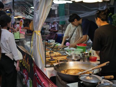 Tayland, Bangkok, Chok Chai 4 Taze Pazar 13 Mayıs 2025 akşamı. Sıradan insanlar akşam yemeği için kızarmış böcekler, pizza ve diğer yiyecekleri alıyorlar..