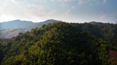 İnsansız hava aracı, yoğun ormanlara karışan ekili tepelerle dağlık arazinin havadan görüntüsünü yakalar. Parlak yeşil yamaçlar, toprak tonlu tepelere ve kısmen de olsa uzak tepelere geçiş