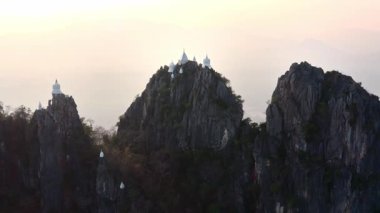 İnsansız hava aracı Wat Chaloem Phra Kiat Tapınağı Kompleksi 'ni beyaz stupalarla bir dağın zirvesinde çeker. Altın ışık sarp kayalıkları ve yeşillikleri vurguluyor. Bu kutsal Tayland Budist 'inde sakin bir atmosfer yaratıyor.