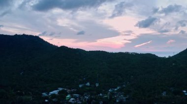 Drone görüntüleri Koh Taos 'un yemyeşil tepeleri ve kıyı günbatımını yakalıyor. Engebeli arazi sonsuz bir okyanusla buluşur. Alacakaranlık renklerini yansıtır. Pembe ve turuncu.