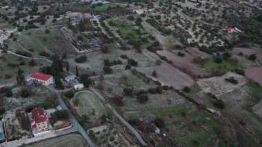 Lefkara köyünün evleri, yolları ve yeşillikleriyle hava manzarası, alacakaranlıkta dağlık araziye geçiş. Yuvarlanan tepeler, vadiler ve gün batımında hafifçe aydınlatılan yuvarlak bir tepe.
