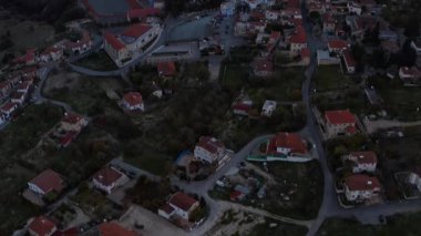 Kıbrıs 'taki Lefkara köyünün alacakaranlıktaki hava aracı görüntülerinde yuvarlanan tepeler arasında kırmızı kiremitli çatılar görülüyor. Bir spor sahası, dolambaçlı bir nehir ve tarihi yerleşim bölgesini çevreleyen yemyeşil bir alan.