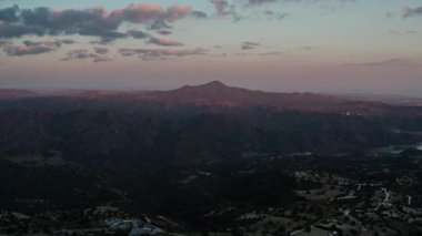 Uçsuz bucaksız dağlık bir arazide dingin bir alacakaranlık. Dalgalanan yeşil tepeler, gökyüzünün altında maviden mora dönüşen belirgin bir zirveye çıkıyor. İnce bulutlar son güneş ışığını yakalıyor.