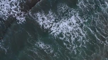 Hava görüntüsü okyanus dalgalarının koyu mavi-yeşil renklere karşı beyaz ibikli olduğunu gösteriyor. Denizin doğal ritmi yakalanır, ışık yansımaları sabah ya da öğleden sonra olduğunu gösterir. Barışçıl bir yukarıdan aşağıya