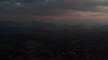 Alacakaranlıkta dumanlı tepeler yuvarlanan arazi ve kasvetli bir gökyüzünün altında sisli dağlar. Tepeler sönen ışıkta parlarken zirveler sislerin içinde saklanır. Lavanta ve şeftali renkleri derinleşen maviler ile harmanlanarak,