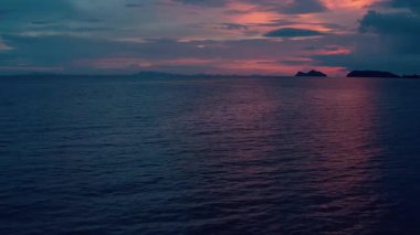 Yumuşak mavi, pembe ve mor renklerle boyanmış bir gökyüzü ile sakin bir alacakaranlık deniz manzarası sakin karanlık denizi yansıtır. Uzak ada siluetleri ufka karıştığında hafif dalgalar dalgalanır.