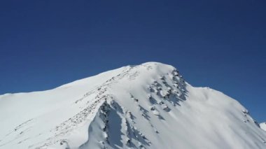 Chegets Dağı 'nın kar kaplı yamaçları, kayalık çıkıntıları ve kayak kaldırma kuleleri olan insansız hava aracı görüntüleri. Kayak izleri güneş ışığı altında el değmemiş karlar arasında zikzak çizerek doğal güzellikleri harmanlıyor.