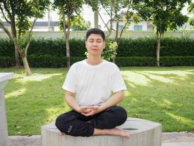 Genç adam parkta yoga yapıyor.