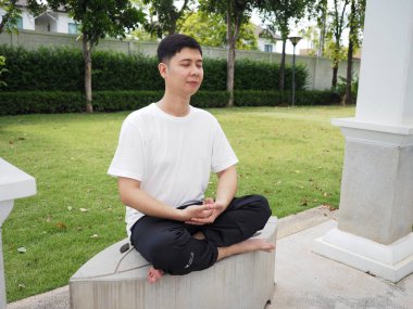 Portre Asyalı adam bahçede oturuyor ve rahatlıyor.