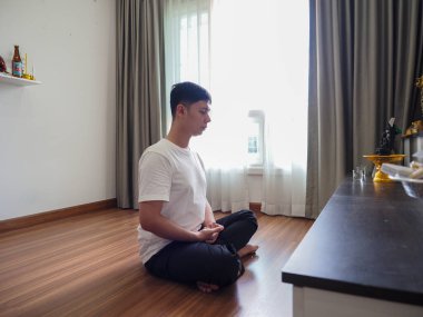 Asyalı adam odada meditasyon yapıyor.