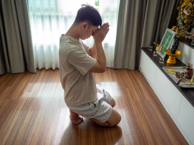 Asyalı bir adam ahşap zeminde eğiliyor. Geleneksel ev ritüelinin ve özel mekanda ruhani uygulamanın bir parçası.