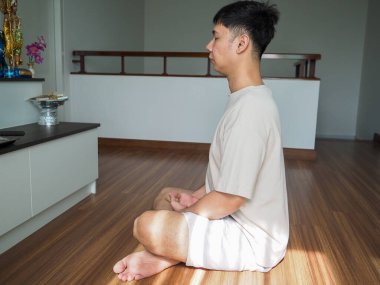 Asyalı bir adamın elinde tütsü çubukları tutarken, diz çökerken, ahşap odada, bir sunağın önünde