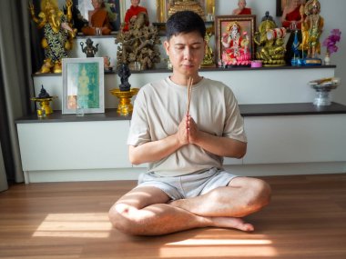 Asyalı bir adam elleri çapraz bağlanmış, sakin bir şekilde dua ediyor, ruhani ev çalışmalarına katılıyor.