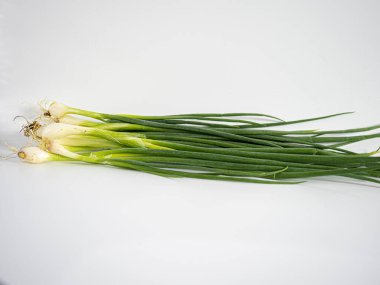 Beyaz yüzeyde üst üste gelen taze soğan demetleri, dışarı doğru kıvrılan yeşil saplar. Bileşimi yiyecek, bitki veya organik içerik için temiz, minimal ve idealdir.