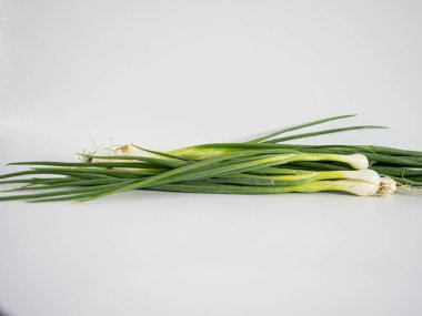 Çerçeve boyunca nazik bir eğri şeklinde dizilmiş bir grup soğan, kökler ve saplar beyaz arkaplanda görünür. Bileşimi yiyecek, bitki veya organik içerik için temiz, minimal ve idealdir.