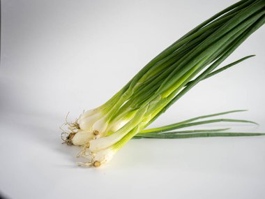 İzole edilmiş taze soğan demeti çapraz eğimli ve minimalist beyaz arka planda güçlü röfleler var. Bileşimi yiyecek, bitki veya organik içerik için temiz, minimal ve idealdir.