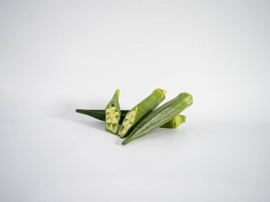 Dilimlenmiş yeşil bamya kabukları yumuşak ışıklandırma altında beyaz bir zemin üzerinde sunuluyor, dokuyu ve tazeliği vurguluyor. Yemek, yemek pişirme veya temiz yemek temaları için ideal.