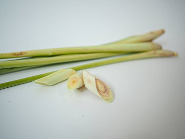Temiz beyaz yüzeyde iki orta boy limon otu sapı. Yumuşak ışıklandırma gıda markalaştırma, aşçılık içeriği veya ürün kullanımı için organik detayları vurgular.