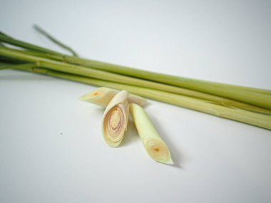 Yakın kesilmiş limon çimleri, beyaz yüzeyde kök ile eşleştirilmiş. Organik veya temiz baharat grafikleri için tazelik ve bitki dokusunu vurgula.