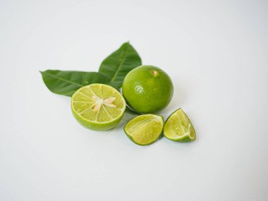  Temiz yemek ve mutfak kompozisyonu için beyaz zemin üzerinde taze yeşil limon ve dilimler sergilenmektedir.