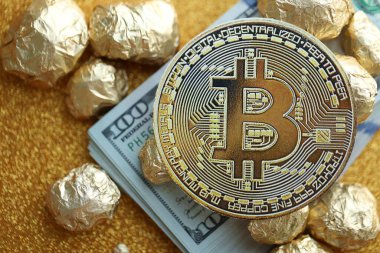 Yüzlerce Amerikan doları üzerinde küçük altın külçeler ve bitcoin kripto para yığını.