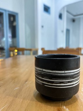 Ahşap masanın üzerinde beyaz çizgili siyah bir seramik bardak. Geceleri sıcak ışıklar ve bulanık bir arka planla rahat bir ortamda..