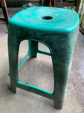 Üzerinde yuvarlak bir delik olan eskimiş yeşil plastik bir tabure, açık havada beton bir zemine yerleştirilmiş..