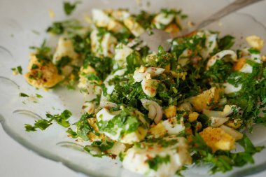 Haşlanmış yumurta ve bol yeşillik. Bir kişi tabağı karıştırıyor.,