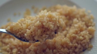 Yeni pişmiş bulgur pilavının üstünde buhar yükseliyor, kaşıkta yakın plan bulgur pilavı.,