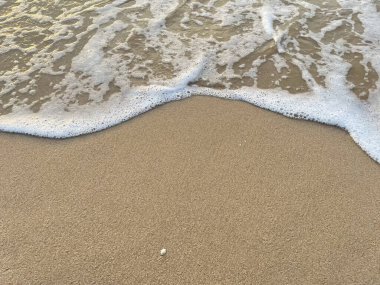 Beyaz köpük dalgaları kumlu sahilde 