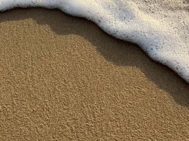 Beyaz köpük dalgaları kumlu sahilde