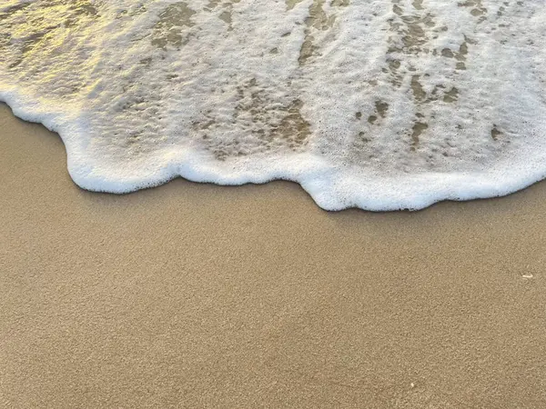 Beyaz köpük dalgaları kumlu sahilde