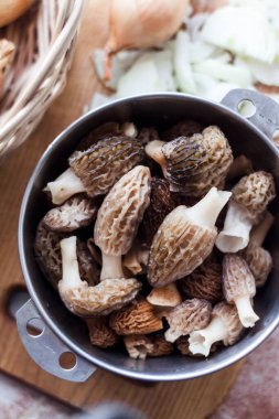 Bahar Morel mantarları ahşap kesme tahtasındaki metal bir kasede. Düz yat, yakın çekim.  