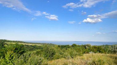 Ukrayna 'nın Çerkasya bölgesindeki Kaniv Barajı' nın geniş manzarası. Parlak mavi bir gökyüzü altında yeşil tepeler ve yemyeşil ormanlar..