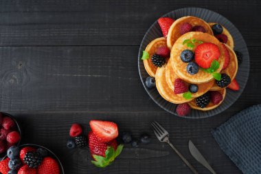 Taze böğürtlenlerle kaplı, siyah ahşap arka planda altın krep düz bir tabaka hoş ve hoşgörülü bir sahne yaratır..