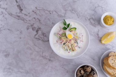 Doğranmış okroshka malzemeleriyle dolu beyaz yuvarlak bir tabak açık gri arka planda göze çarpar..